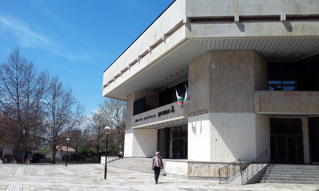 Dom Kultury „Arsenal” w Kazanłyku, masywny betonowy budynek w stylu socrealistycznym, z flagami przed wejściem i placem przed nim.